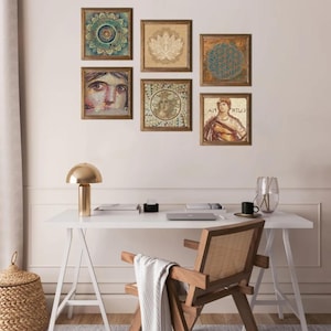 May include: A collection of framed art pieces with various designs, including a mandala, lotus flower, and geometric patterns. The artwork is displayed on a light-colored wall above a white desk with a gold lamp and wooden chair.