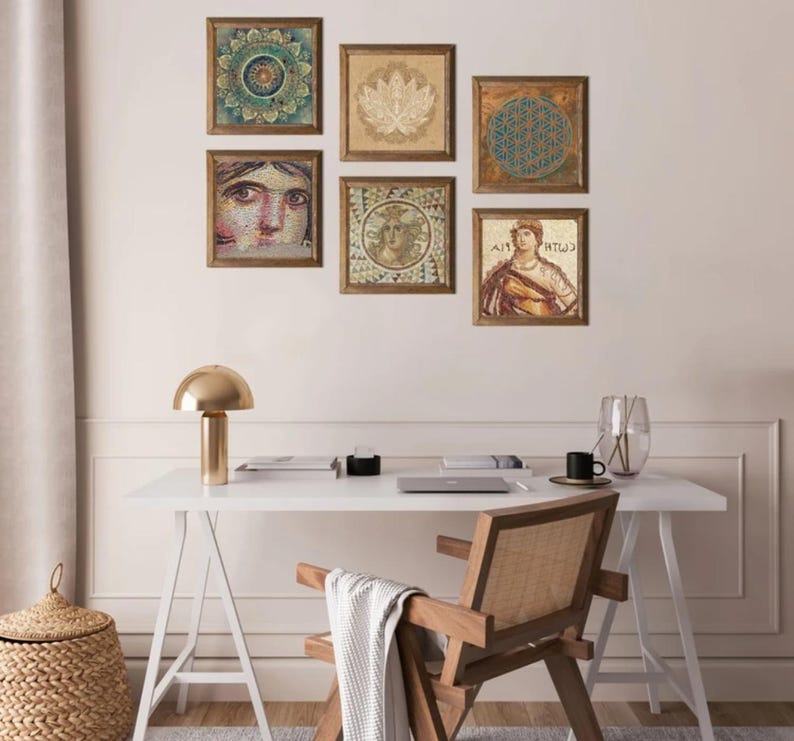 May include: A collection of framed art pieces with various designs, including a mandala, lotus flower, and geometric patterns. The artwork is displayed on a light-colored wall above a white desk with a gold lamp and wooden chair.