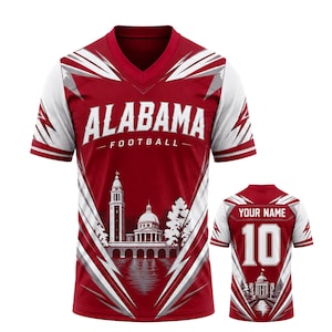 Peut inclure: Un maillot à col en V rouge cramoisi et blanc avec le texte ALABAMA FOOTBALL sur le devant et un graphique de bâtiment à dôme. Le dos affiche le texte YOUR NAME au-dessus du numéro 10 et un graphique plus petit du même bâtiment.