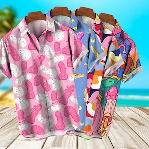 May include: Four short-sleeved button-down shirts with unique patterns. The shirts feature designs in pink, blue, and multi-colored patterns. The background shows a beach scene with a wooden surface.
