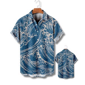 Op de afbeelding: Blauw overhemd met korte mouwen en een golfpatroon. Het overhemd heeft een knoopsluiting en een klassieke kraag. Een tweede overhemd wordt op een hanger getoond, met de achterkant van het overhemd.