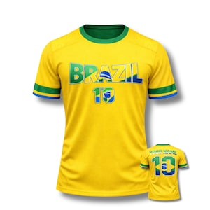 Może przedstawiać: Ż&oacute;łta koszulka piłkarska Brazylii z zielonymi i niebieskimi akcentami. Słowo "BRAZIL" jest na piersi w kolorze zielonym i niebieskim, z numerem "10" poniżej. Mniejsza wersja koszulki jest widoczna w prawym dolnym rogu.