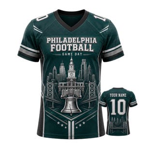Könnte beinhalten: Ein dunkelgrünes Football-Trikot mit dem Text "PHILADELPHIA FOOTBALL GAME DAY" und einer Grafik der Skyline von Philadelphia, der Liberty Bell und Brücken. Das Trikot hat weiße und silberne Akzente und die Nummer "10".