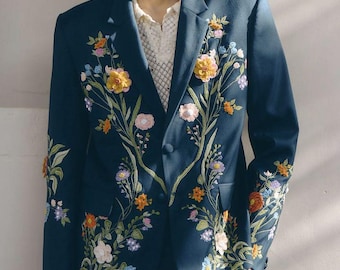 Könnte beinhalten: Ein dunkelblauer Blazer mit farbenfroher Blumenstickerei. Die Jacke hat einen Zwei-Knopf-Verschluss und ist mit gestickten Blumen in Gelb-, Orange-, Rosa- und Blautönen verziert, wodurch ein lebendiges und künstlerisches Design entsteht.