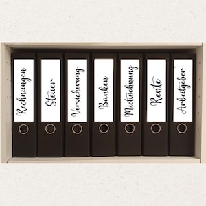 Könnte beinhalten: Ein Regal mit sieben schwarzen Ordnern. Jeder Ordner hat ein weißes Etikett mit schwarzem Schreibschrifttext. Die Etiketten lauten: "Rechnungen", "Steuer", "Versicherung", "Banken", "Mietwohnung", "Rente" und "Arbeitgeber".