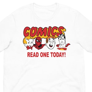 Può includere: T-shirt bianca con la scritta "COMICS" in rosso e giallo, con illustrazioni di personaggi dei fumetti. Sotto la parola "COMICS" c'è la scritta "READ ONE TODAY!".