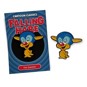 Könnte beinhalten: Ein Cartoon-Pin und Karten-Set mit einem Charakter aus "Falling Hare". Der Pin ist ein gelber und blauer Gremlin mit roter Nase. Die Karte trägt den Text "Cartoon Classics Falling Hare" und "The Gremlin".