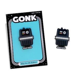 May include: A black and grey GONK droid pin and matching card. The card has a light blue background with the word "GONK" in white. The card also has the text "May the 4th Edition" and "Ages 4 and up".