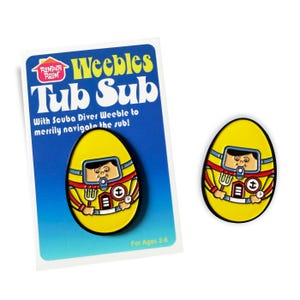 Puede incluir: Un juguete amarillo Weeble Tub Sub con un diseño de buzo. El juguete en forma de huevo tiene un contorno negro y el texto "Weebles Tub Sub" y "For Ages 2-6". El juguete está sobre una tarjeta azul y blanca.