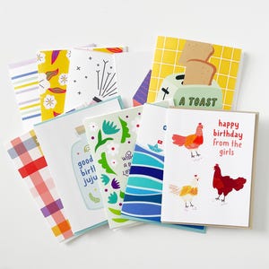 May include: A collection of assorted greeting cards featuring various illustrations including a toaster with toast labeled A TOAST, a bottle with text, a boat on blue waves, and three chickens with the text happy birthday from the girls.