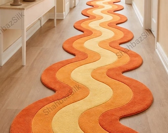 May include: A long, wavy rug in shades of orange and yellow, creating a retro, eye-catching design. The rug is placed in a hallway with light-colored walls and wooden flooring. The rug's dimensions are not visible.