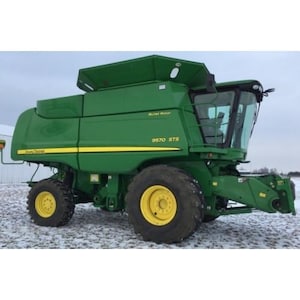 Może przedstawiać: Zielony kombajn John Deere 9570 STS z żółtymi akcentami. Duża maszyna rolnicza ma kabinę z oknami i duże opony. Kombajn stoi na zaśnieżonym polu.
