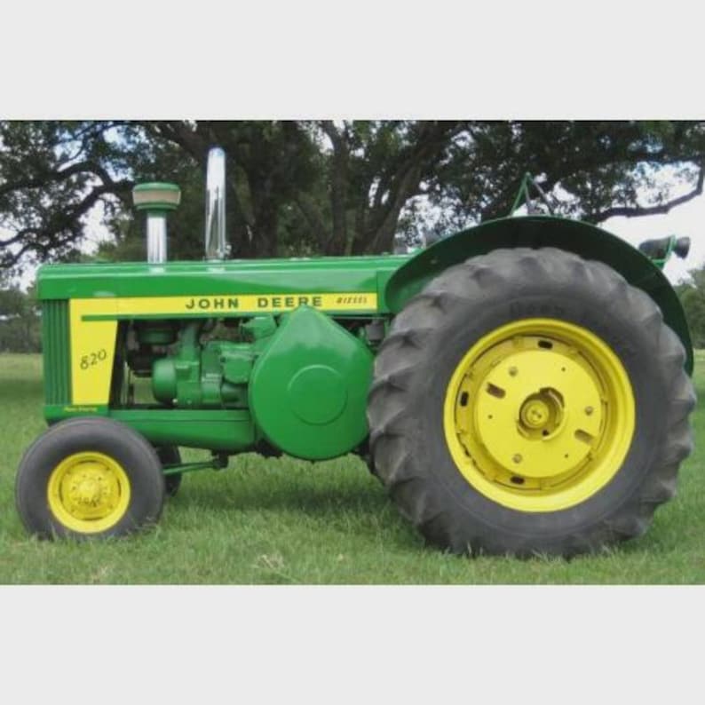 Może przedstawiać: Zabytkowy traktor John Deere 820, w kolorze zielono-ż&oacute;łtym. Traktor posiada duże czarne opony z ż&oacute;łtymi felgami, srebrną rurę wydechową i logo John Deere z boku.