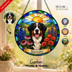 May include: A circular stained glass suncatcher featuring a Bernese Mountain Dog portrait, a sunlit landscape, and colorful flowers. A banner at the bottom displays the name Barnaby. The piece is suspended by a black metal chain for display.