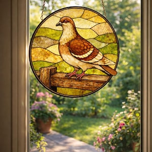 May include: A round stained glass window hanging featuring a brown and white bird perched on a wooden fence. The background is a landscape of green and yellow fields. The window is suspended by a gold chain.