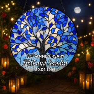 Può includere: Un vetro colorato rotondo con un disegno di albero, foglie blu e un tronco marrone. Il testo "30th ANNIVERSARY Phil and Sandra 20.09.1995" è presente. Appeso a una catena.
