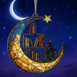 May include: A crescent moon-shaped hanging ornament featuring a stained glass design with a gradient of yellow, orange, and blue. It includes a small bookshelf filled with books and a black cat sitting on the moon, topped with a yellow star.