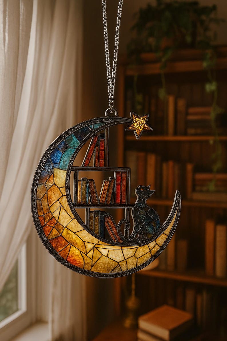May include: A crescent moon-shaped suncatcher featuring a stained glass mosaic design in shades of blue, orange, and yellow. The piece includes a built-in bookshelf with miniature books and a cat silhouette, topped with a small yellow star.