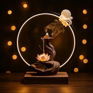 Peut inclure: Un brûleur d'encens en céramique marron avec un motif de fleur de lotus, dégageant de la fumée. Le brûleur est sur une base en bois, avec un anneau lumineux et des lumières décoratives en arrière-plan. Une figurine blanche en forme de poulpe est au sommet.