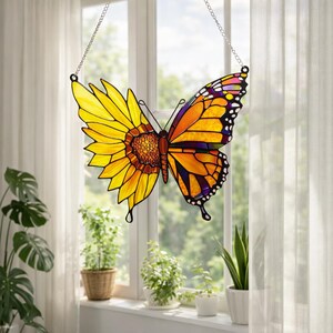 May include: Stained glass butterfly suncatcher with a sunflower design on one wing and a monarch butterfly design on the other. The butterfly is suspended by a silver chain. The colors include yellow, orange, brown, purple, and white.