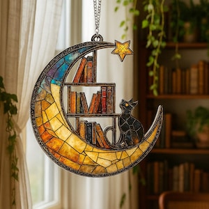 May include: A crescent moon-shaped stained glass suncatcher featuring a multi-colored mosaic pattern, a built-in bookshelf with various books, a black cat silhouette, and a small yellow star accent, all suspended by a silver-toned metal chain.