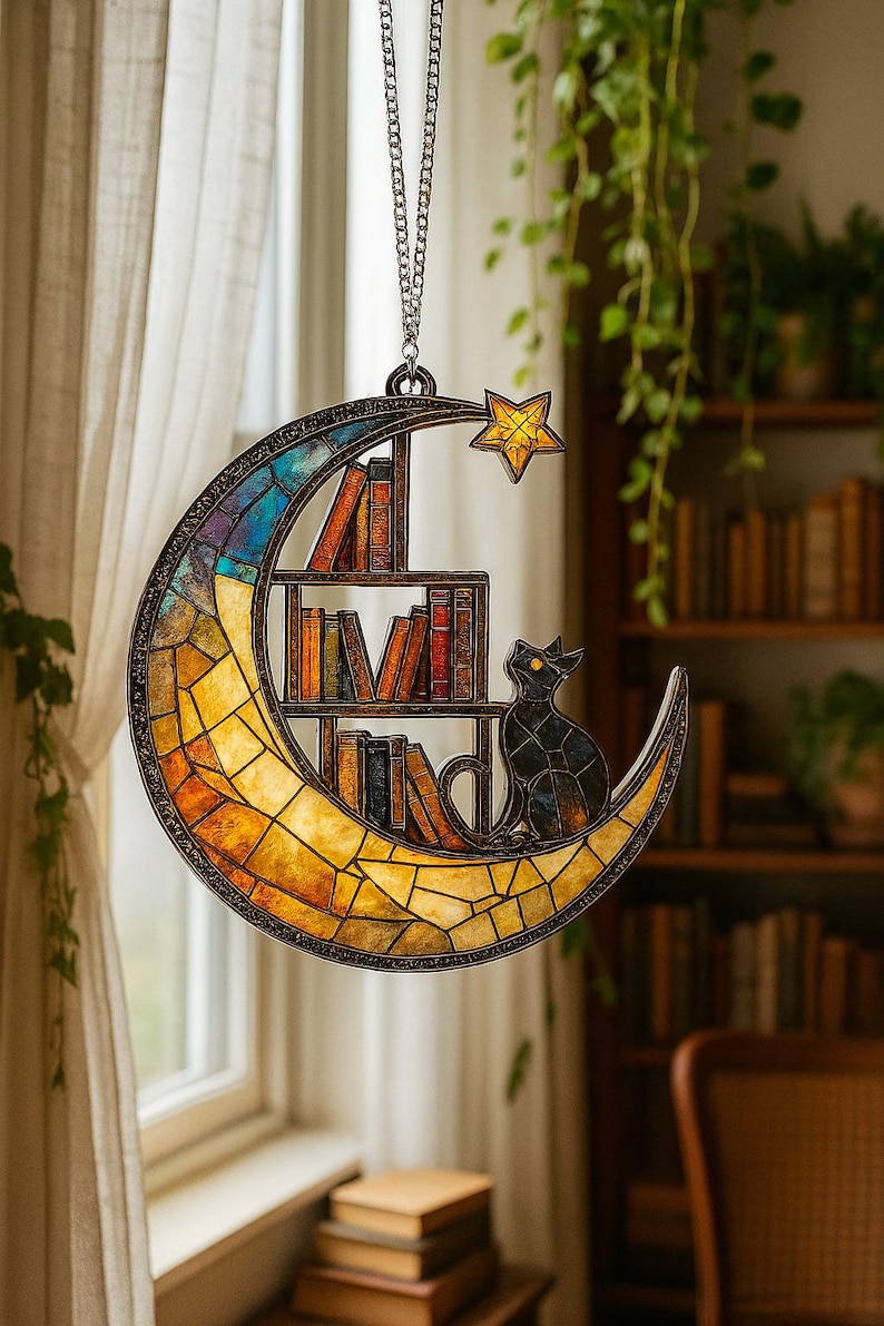 May include: A crescent moon-shaped stained glass suncatcher featuring a multi-colored mosaic pattern, a built-in bookshelf with various books, a black cat silhouette, and a small yellow star accent, all suspended by a silver-toned metal chain.
