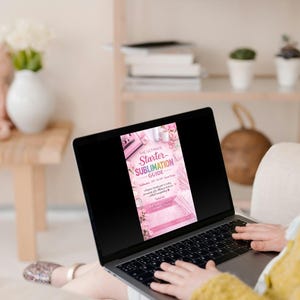 Op de afbeelding: Een laptop met een roze en witte gids met de titel "The Ultimate Starter Sublimation Guide". Het scherm toont een bloemmotief met tekst. De laptop is open en de gebruiker typt op het toetsenbord. De achtergrond omvat een bank met knuffels en een vaas met bloemen.