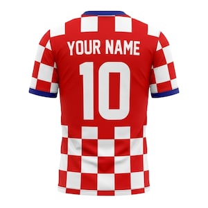 May include: Red soccer jersey with white checkered pattern on the shoulders and lower section. The jersey features the number 10 in white and the text "YOUR NAME" above it. The collar and sleeve cuffs are blue.