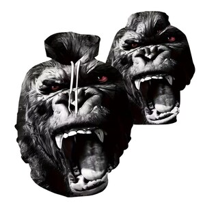 May include: A black and white hooded sweatshirt featuring a large, detailed graphic print of a gorilla with an open mouth, bared teeth, and glowing red eyes. The hoodie includes a drawstring hood and a realistic, high-contrast animal portrait design.