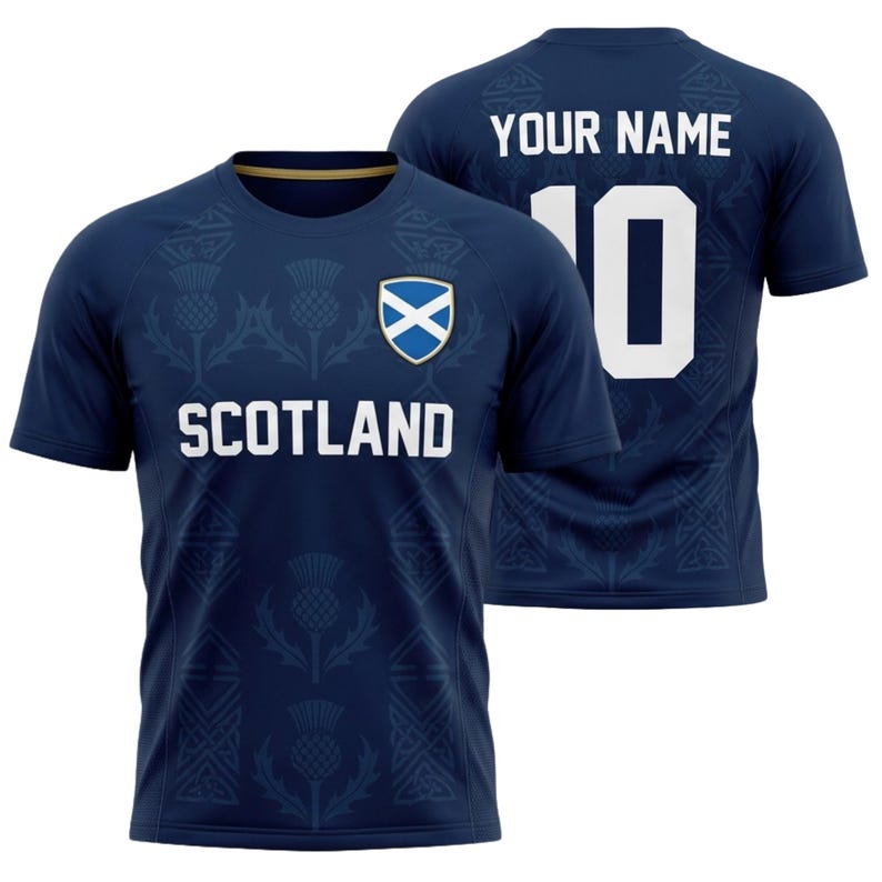 May include: Navy blue Scotland soccer jersey with white text and a team crest. The front of the shirt displays "SCOTLAND" and a crest. The back features "YOUR NAME" above the number "10". The jersey has a thistle pattern.