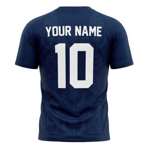 May include: Navy blue short-sleeve jersey with the text "YOUR NAME" above the number "10" in white. The jersey has a thistle pattern and a Celtic knot design. A sports-themed apparel item.