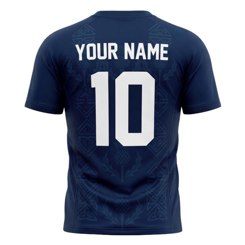 May include: Navy blue short-sleeve jersey with the text "YOUR NAME" above the number "10" in white. The jersey has a thistle pattern and a Celtic knot design. A sports-themed apparel item.