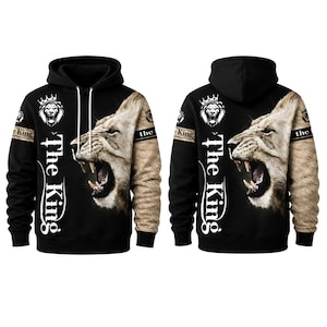 Peut inclure: Un sweat-shirt à capuche noir avec un grand graphique réaliste d'une tête de lion rugissant sur le devant. Le texte "The King" est imprimé verticalement en lettres blanches à côté du lion. Les manches ont un motif de fourrure beige.