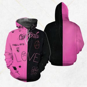 Op de afbeelding: Roze en zwarte hoodie met de tekst "Cry Baby" en andere afbeeldingen. De hoodie is in het midden gesplitst, met de linkerkant roze en de rechterkant zwart. De hoodie heeft een capuchon en een trekkoord.