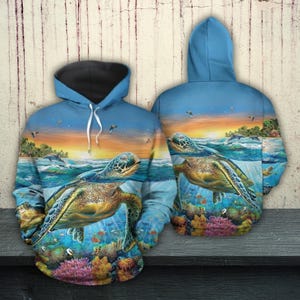 May include: A blue hoodie featuring a vibrant ocean scene with sea turtles, coral, and fish. The design includes a sunset, dolphins, and birds, creating a colorful and detailed aquatic theme. The hoodie has a black-lined hood.
