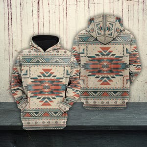 Könnte beinhalten: Ein beigefarbener Kapuzenpullover mit einem geometrischen Muster im Südwesten in Türkis, Rot und Schwarz. Der Kapuzenpullover hat eine schwarz gefütterte Kapuze und ein passendes Muster auf der Vorder- und Rückseite. Das Design zeigt Dreiecke, Linien und Rauten.