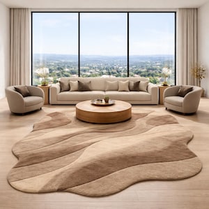 Op de afbeelding: Een moderne woonkamer met een beige bank, twee fauteuils en een ronde houten salontafel. Een groot, abstract gevormd tapijt in bruin- en beigetinten bedekt de vloer. Grote ramen bieden een schilderachtig uitzicht op een groen landschap.