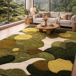 May include: An abstract patterned rug in a living room. The rug features overlapping shapes in shades of green, yellow, and cream. The room also includes a neutral-toned sofa, wooden coffee table, and large windows overlooking a forest.