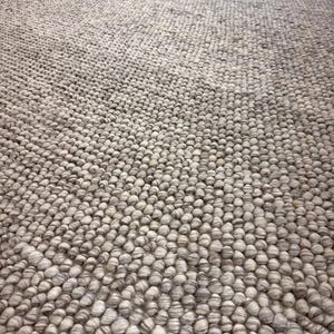 May include: A textured area rug featuring a dense, uniform pattern of small, rounded, felted wool-like spheres in varying shades of light gray, beige, and off-white, creating a tactile, pebble-like surface across the entire rectangular floor covering.