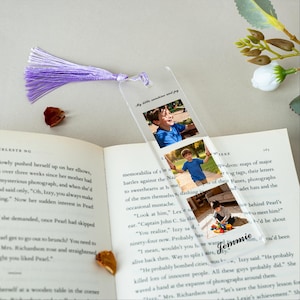 May include: Clear acrylic bookmark with a purple tassel. The bookmark features three photos of a child and the text "My little sunshine and joy" and "Jemmie". The bookmark is placed on an open book.