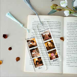 May include: A clear acrylic bookmark with a tassel, featuring a series of small photos. The photos show a young girl in various settings. The bookmark is placed in an open book with text.