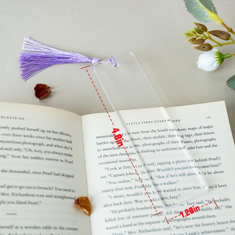 May include: A clear, rectangular bookmark with a purple tassel, measuring 4.8 inches long and 1.28 inches wide. The bookmark is placed on an open book. The tassel is made of multiple strands of purple thread.
