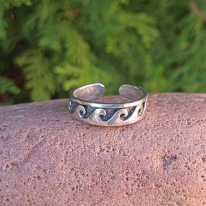 May include: Silver toe ring with a wave design. The ring is open and adjustable.