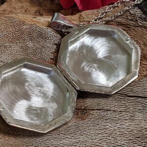 May include: An open silver locket with an octagonal shape. The locket is made of polished metal and has a hinged lid.