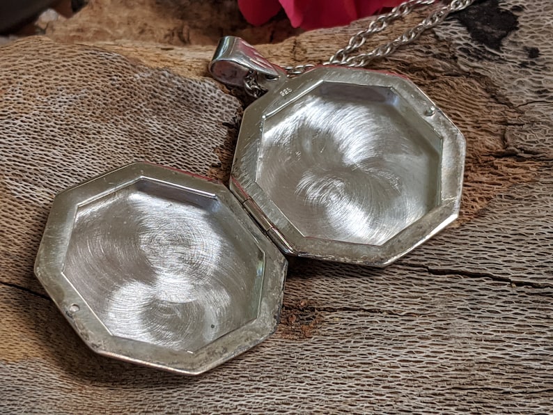 May include: An open silver locket with an octagonal shape. The locket is made of polished metal and has a hinged lid.