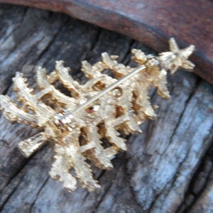 May include: A gold-toned Christmas tree brooch with a star on top. The textured metal design features a pin on the back for secure attachment. This festive accessory is perfect for holiday celebrations and adding a touch of sparkle to any outfit.