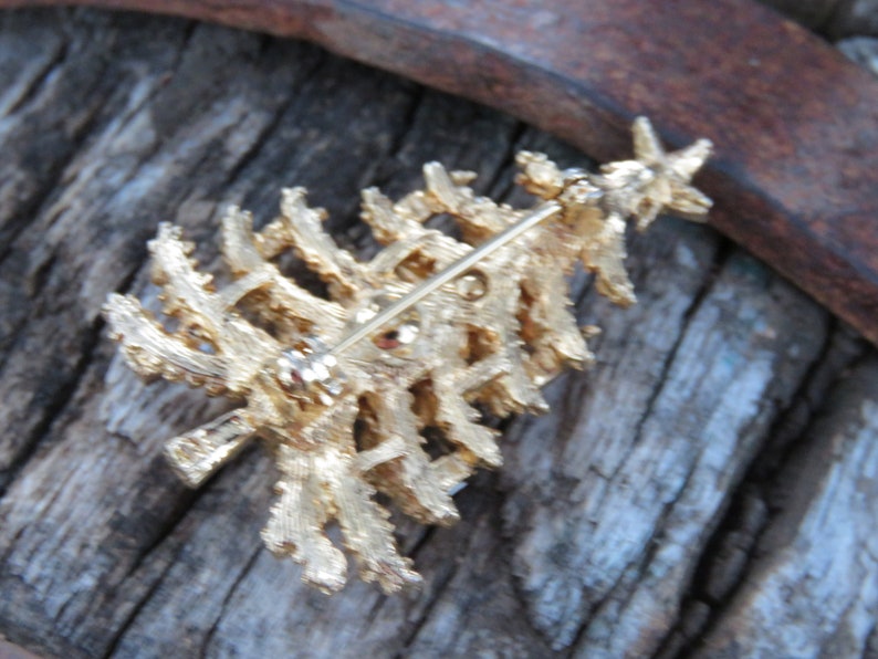 May include: A gold-toned Christmas tree brooch with a star on top. The textured metal design features a pin on the back for secure attachment. This festive accessory is perfect for holiday celebrations and adding a touch of sparkle to any outfit.
