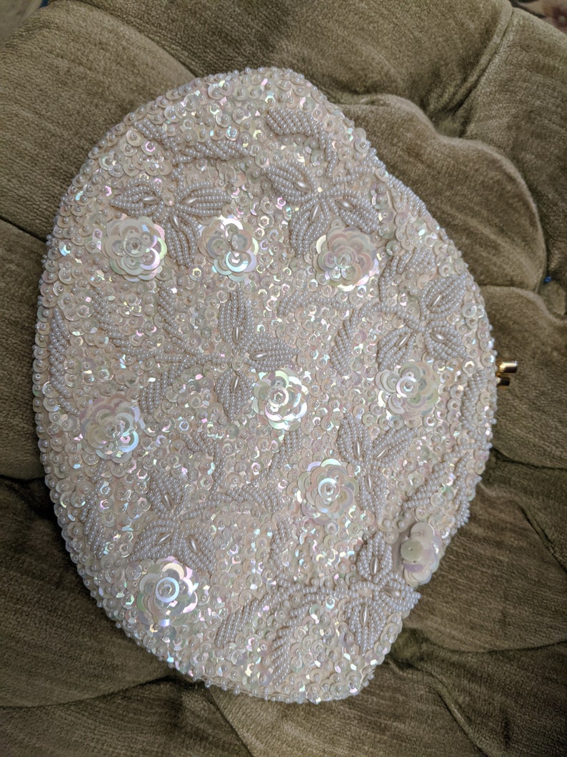 Puede incluir: Un bolso de mano blanco de cuentas con un dise&ntilde;o floral. El bolso est&aacute; cubierto de lentejuelas iridiscentes y peque&ntilde;as cuentas blancas.