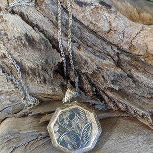 May include: A silver locket necklace with a detailed floral design. The locket is octagonal in shape and hangs from a silver chain.