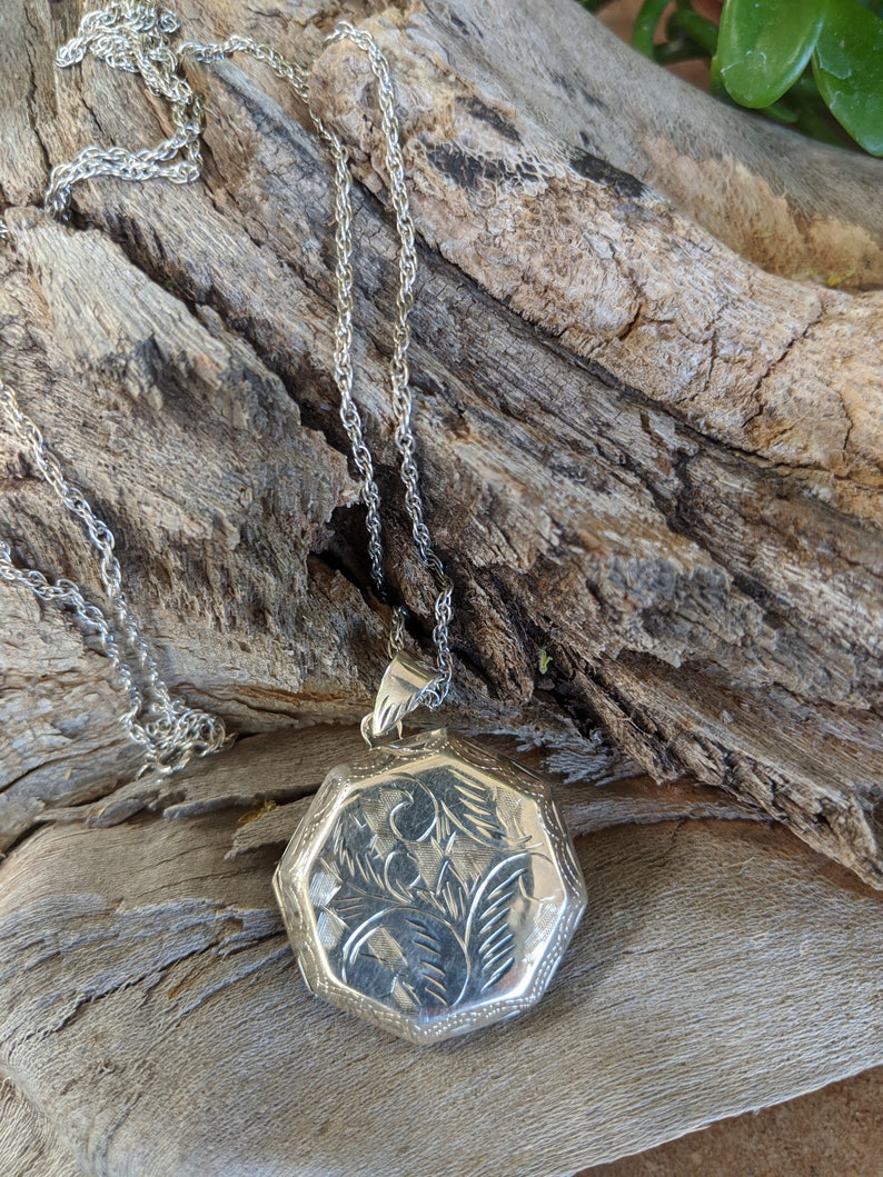 May include: A silver locket necklace with a detailed floral design. The locket is octagonal in shape and hangs from a silver chain.